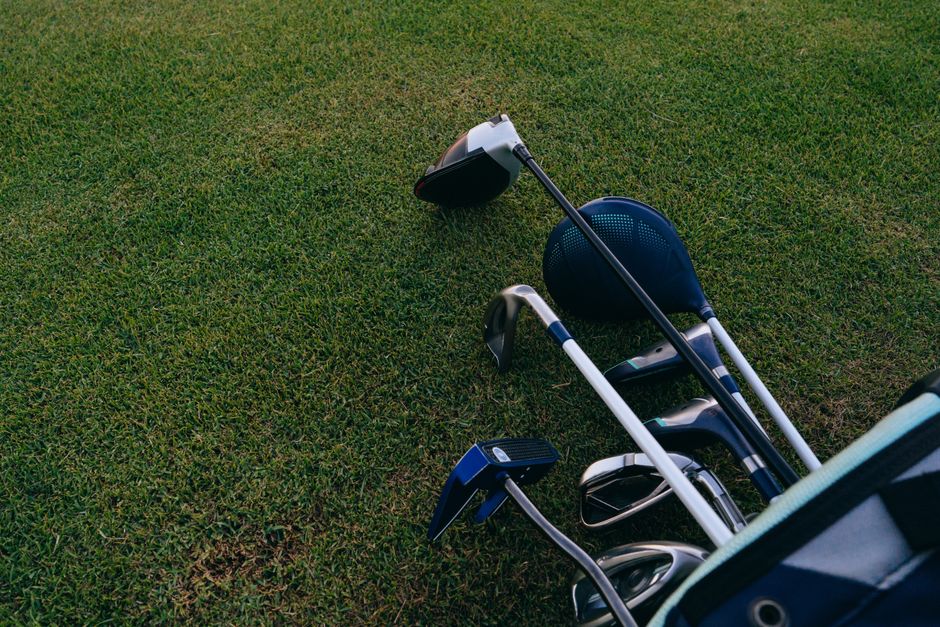 Imagem de um conjunto de tacos de golfe e acessórios dispostos em um campo gramado, ideal para destacar o tema de esportes ou lazer ao ar livre.