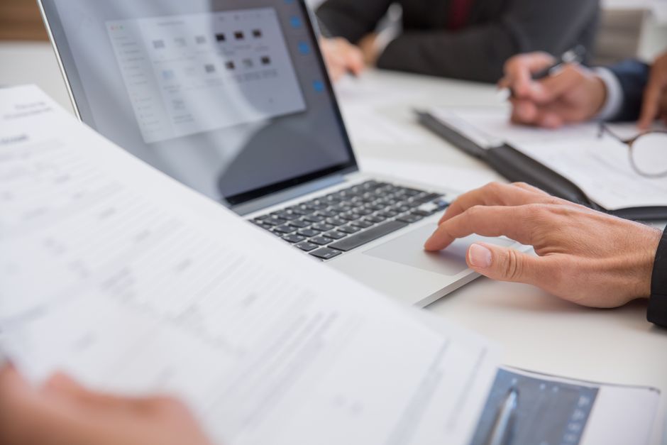 Pessoa realizando análise de dados financeiros utilizando um laptop em ambiente de escritório.