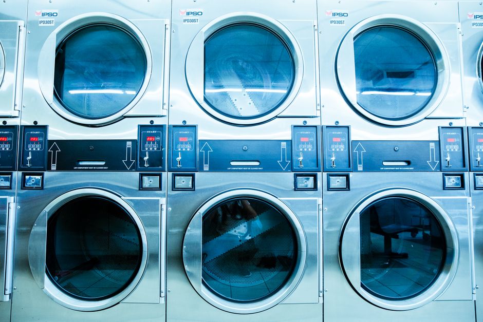 Lavanderia industrial com máquinas de lavar roupa empilhadas, destacando o ambiente de limpeza e manutenção de roupas em estabelecimentos comerciais.