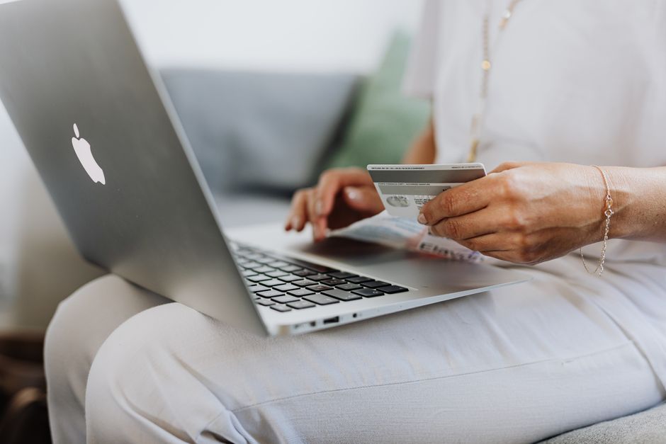 Pessoa realizando uma transação online utilizando um laptop e cartão de crédito, representando compras digitais ou gerenciamento financeiro digital.