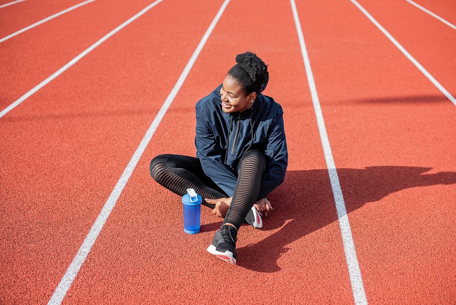 Atleta feminina descansando após treino na pista de corrida ao ar livre, sorrindo relaxada.