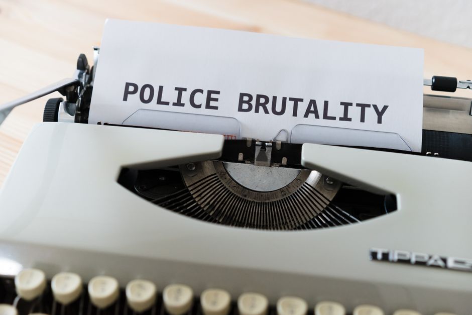 Imagem de uma máquina de escrever com uma folha que exibe a frase 'POLICE BRUTALITY', abordando temas de justiça, direitos humanos e repressão policial.