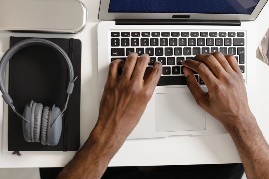 Imagem de uma pessoa usando um computador portátil em um ambiente de trabalho ou estudo, com fones de ouvido ao lado, representando atividades relacionadas a tecnologia e produtividade.