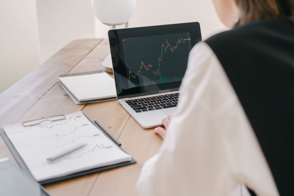 Pessoa analisando gráficos de mercado financeiro em um ambiente de trabalho, enfatizando estratégias de investimento.
