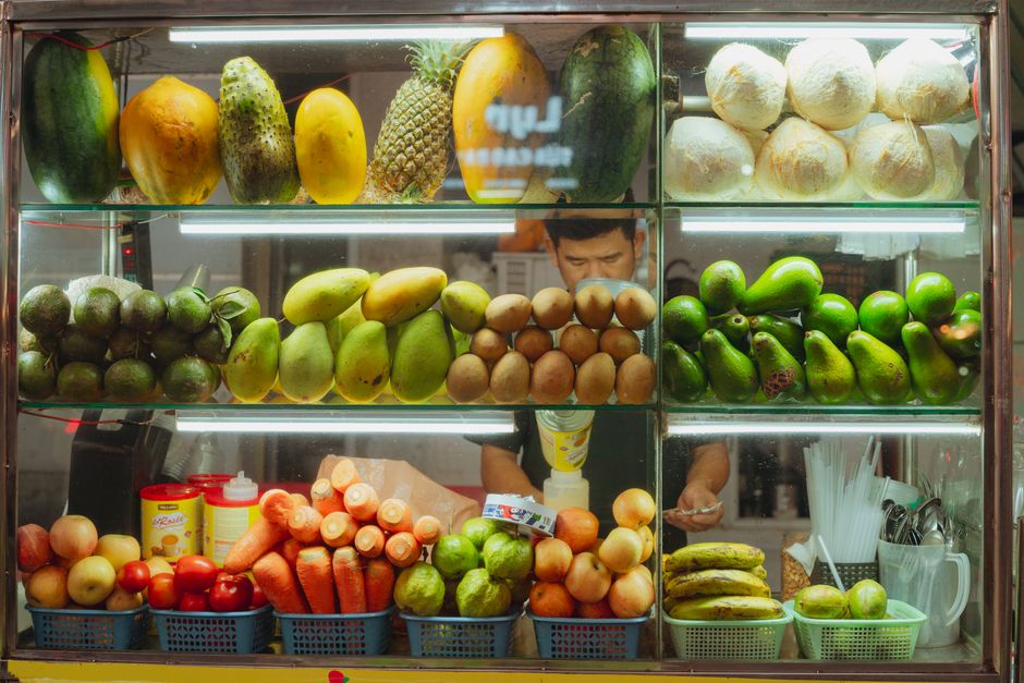 Vendedor de frutas em uma bancadinha de mercado, exibindo uma variedade de frutas frescas ao público.