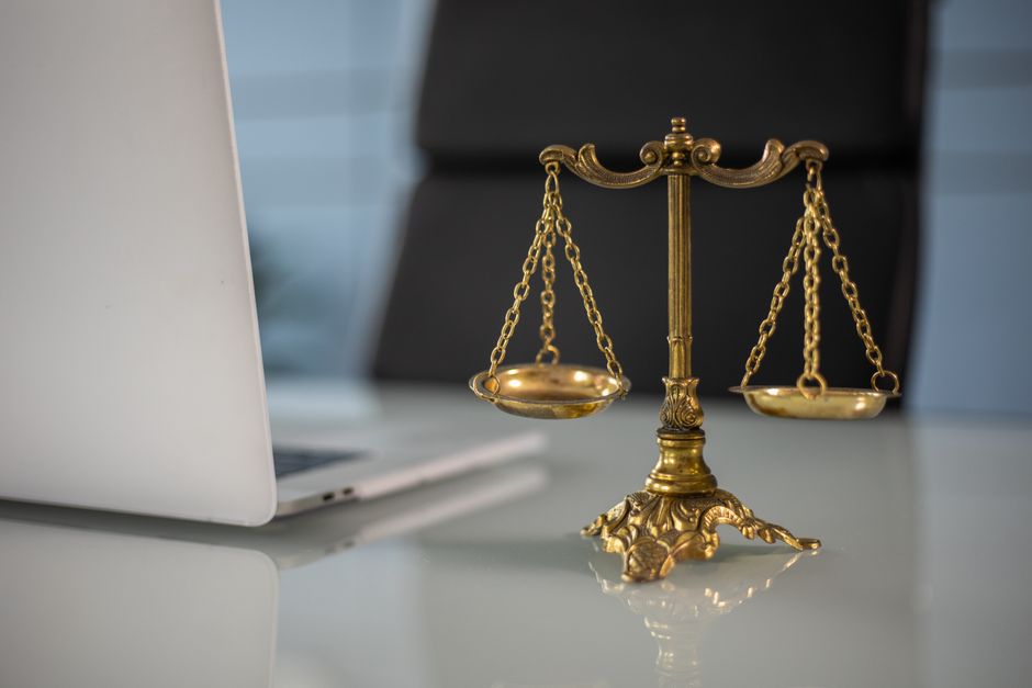 Balança de justiça dourada sobre mesa de escritório ao lado de um computador, simbolizando equilíbrio, ética e legalidade nos negócios.