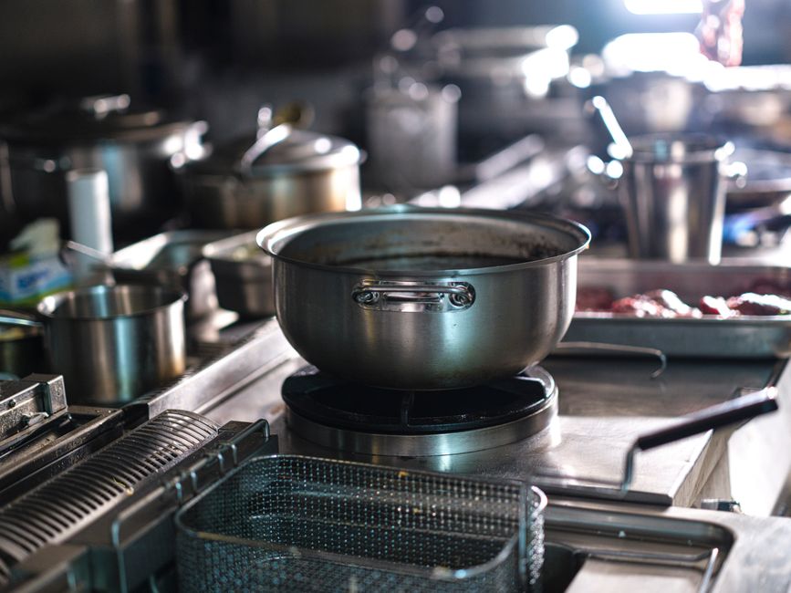 Imagem de uma cozinha industrial com utensílios de cozinha e panelas, destacando uma área de preparo de alimentos em um ambiente profissional.