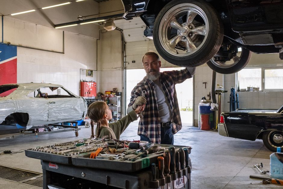 Imagem de um mecânico e uma criança trocando um aperto de mão em um auto center, simbolizando colaboração e educação técnica na manutenção de veículos.