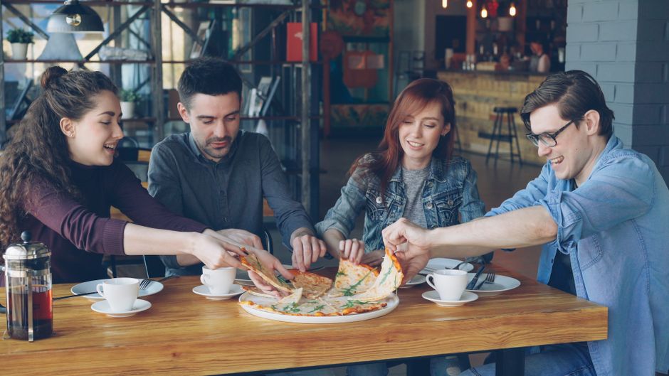 Grupo de amigos compartilhando uma pizza em um ambiente descontraído, simbolizando socialização e lazer.