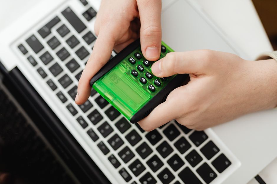 Pessoa usando uma calculadora ao lado de um laptop, simbolizando análise financeira ou contábil.