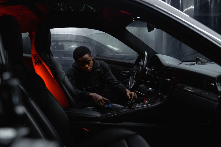Imagem de um jovem sentado no banco do motorista de um carro esportivo com interior moderno, em ambiente urbano, transmitindo sensação de velocidade e inovação.