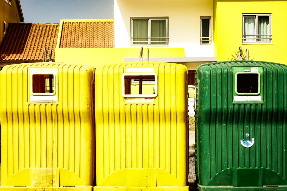 Contêineres de coleta de lixo coloridos na frente de uma residência moderna, destacando a questão da gestão de resíduos urbanos.