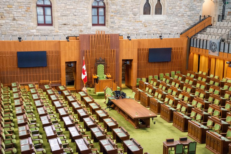 Salão de assembleia governamental com assentos em madeira, palco com tribuna e arranjos tradicionais, ideal para discussões políticas ou debates legislativos.