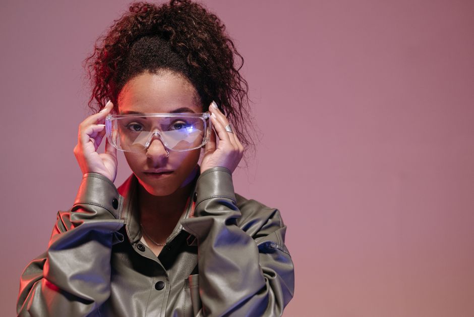 Mulher jovem ajustando óculos de proteção em um ambiente com iluminação colorida, representando inovação e tecnologia.