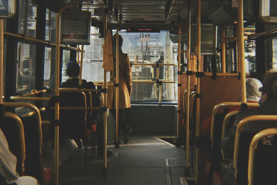 Interior de um ônibus urbano com passageiros sentados e uma pessoa em pé na entrada, ilustrando o transporte público na cidade.