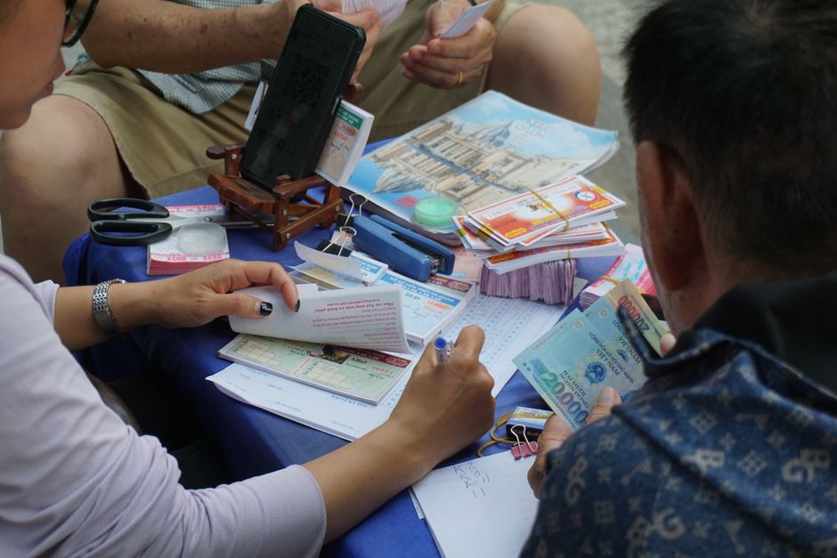 Grupo de pessoas realizando planejamento financeiro ou avaliação de investimentos com documentos, dinheiro e tecnologia em um ambiente colaborativo.