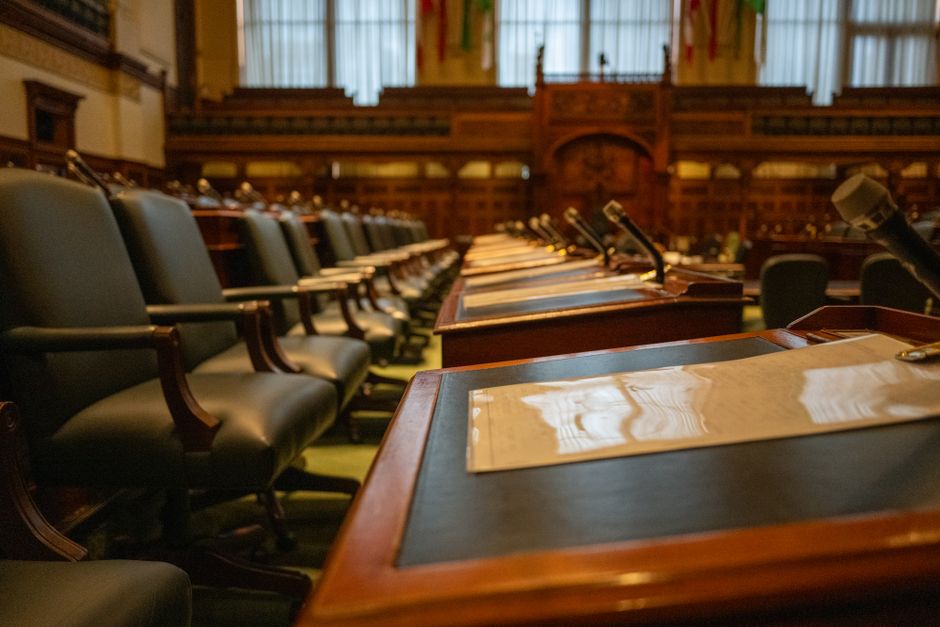 Salão de audiência ou parlamento com cadeiras de couro e mesas de madeira, preparado para uma sessão oficial ou reunião política.