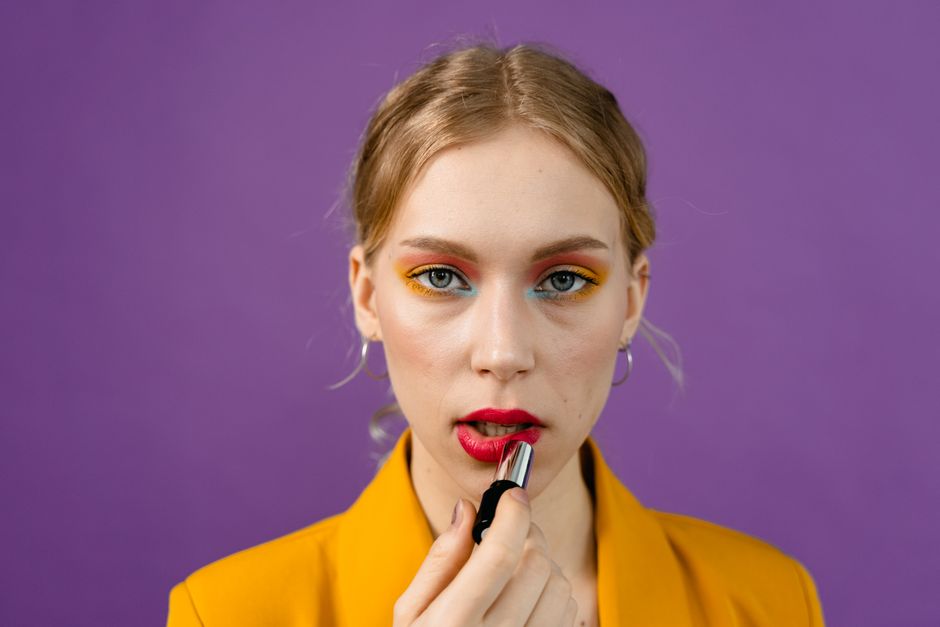Mulher aplicando batom em um fundo roxo, destacando o tema de maquiagem e beleza feminina.