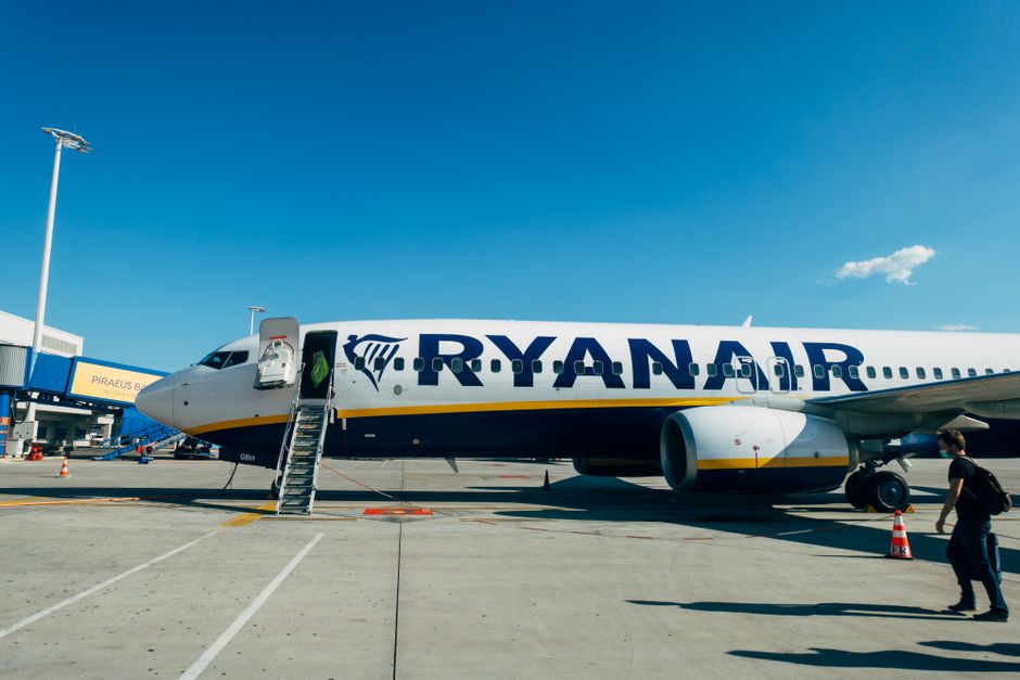 Avião da Ryanair no aeroporto pronto para embarque, com céu claro ao fundo e passageiros entrando na aeronave.