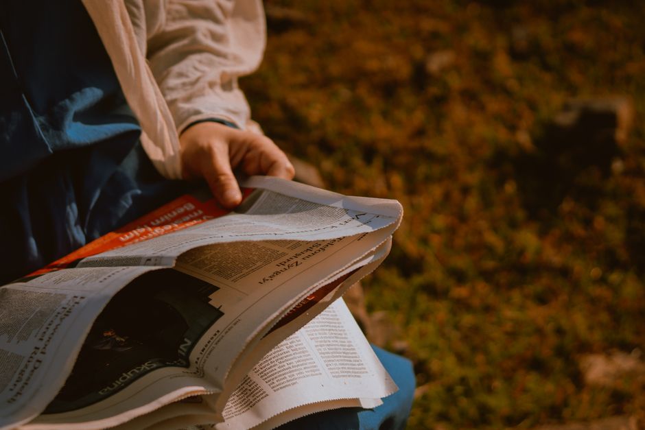 Pessoa lendo jornal ao ar livre, com foco em notícias e atualidades.