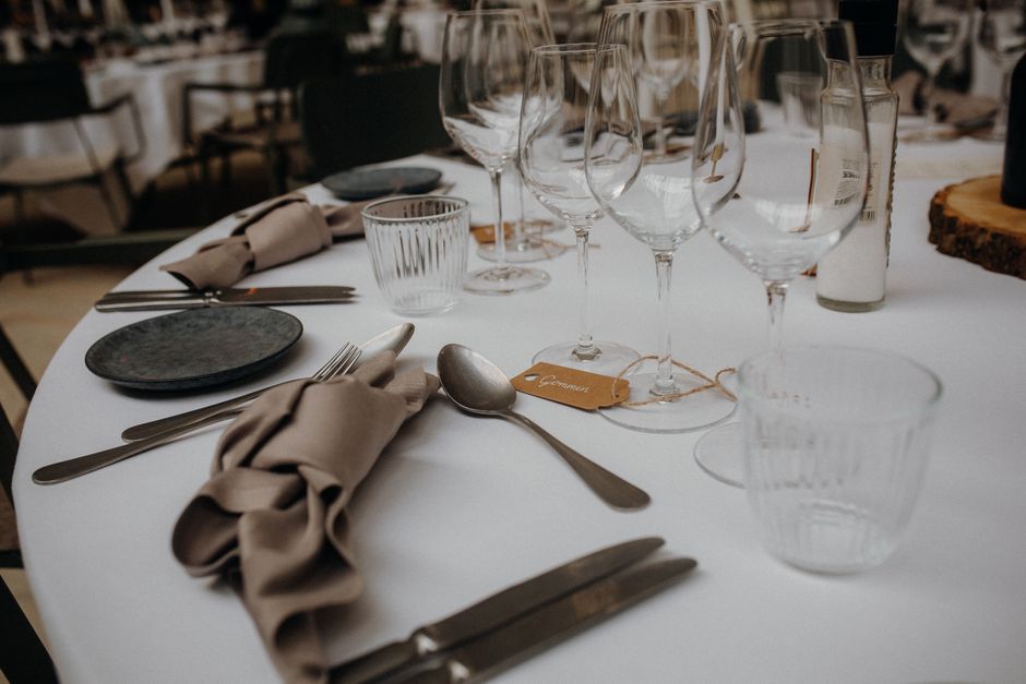 Mesa de evento ou celebração elegante, preparada com copos, talheres e toalhas, ideal para um blog sobre organização de eventos ou cozinhas sofisticadas.