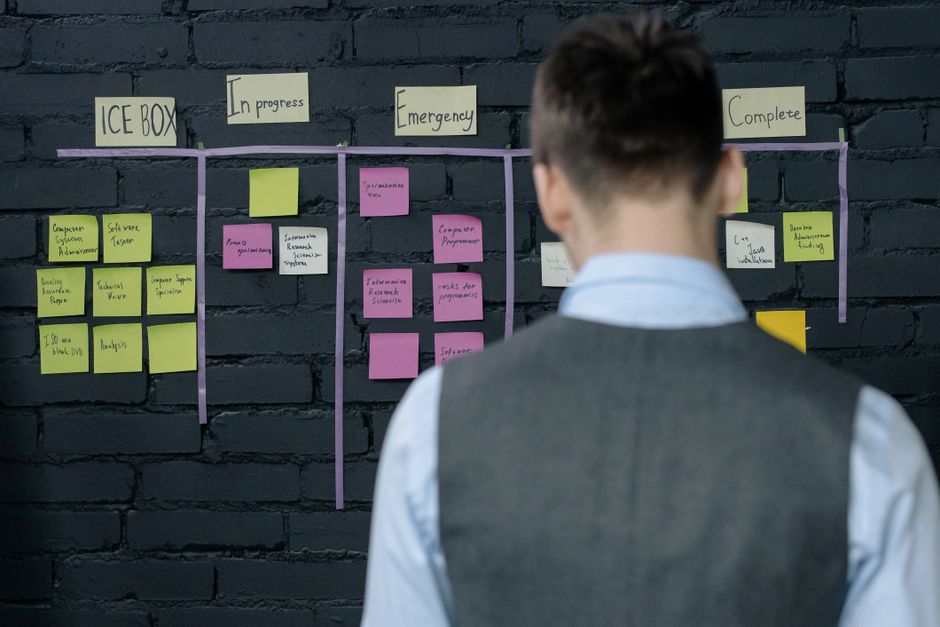 Pessoa analisando um quadro de planejamento e organização de tarefas em um ambiente de trabalho profissional.