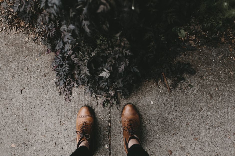 Imagem de um ponto de vista de quem está caminhando por uma calçada, com plantas ao lado, capturando o momento de passeio ao ar livre.