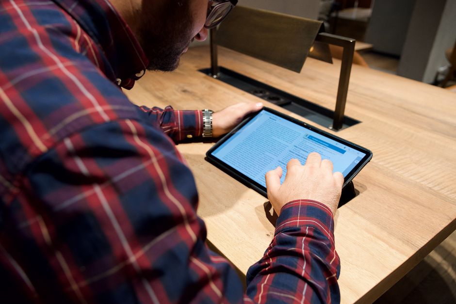 Pessoa utilizando um tablet para leitura ou análise de informações, em ambiente de trabalho colaborativo.