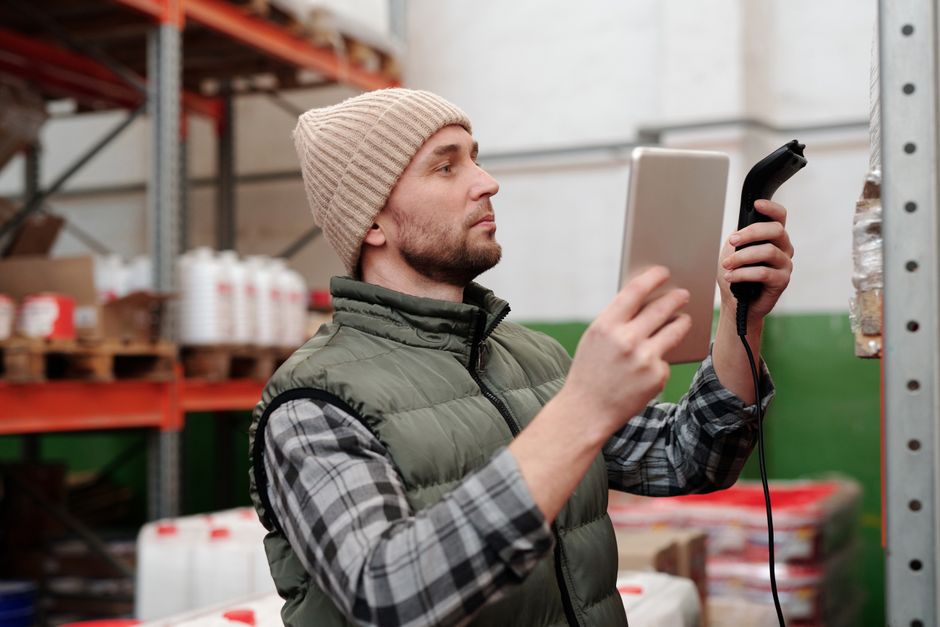 Homem verificando inventário ou produto em estoque usando dispositivo eletrônico em ambiente industrial ou de armazenamento.