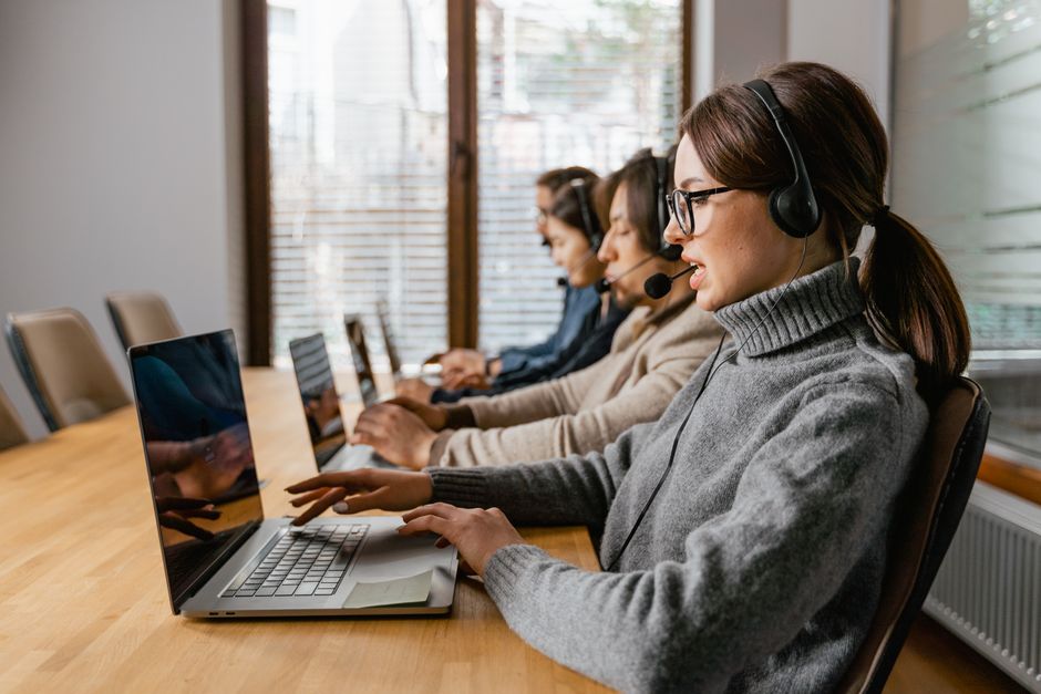 Mulheres trabalhando em um call center com fones de ouvido, realizando atendimento ao cliente em ambiente de escritório.