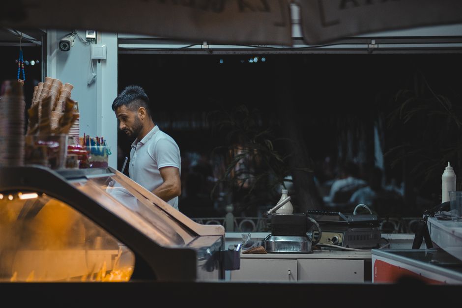 Homem trabalhando em uma sorveteria ao entardecer, destacando a rotina de atendimento ao cliente e produção de sorvetes.