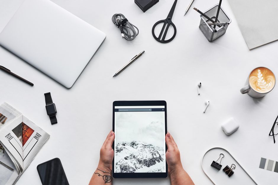 Imagem de uma mesa de trabalho moderna com uma pessoa segurando um tablet com uma paisagem de montanhas e neve, ideal para um artigo sobre produtividade ou inovação no ambiente de trabalho.