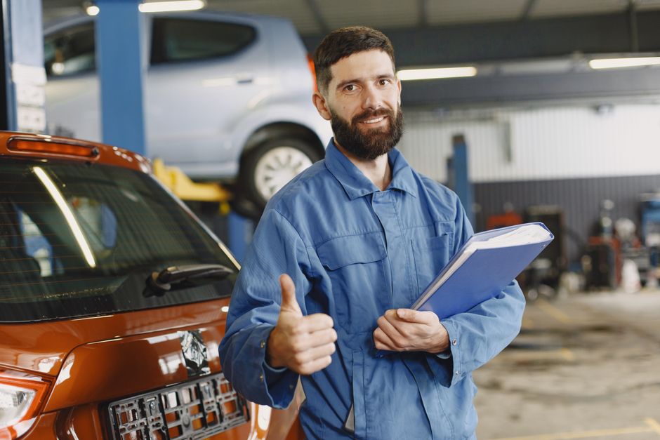 Homem técnico de automóveis sorrindo em oficina, demonstrando confiança e satisfação com o trabalho realizado.