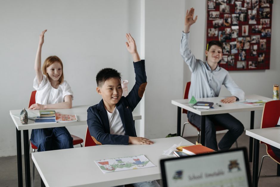 Crianças participando de uma aula interativa com alunos levantando as mãos em um ambiente escolar bonito e bem equipado.