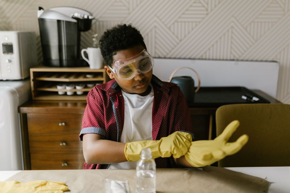 Jovem preparando-se para fazer experimentos científicos em um ambiente doméstico ou escolar, usando equipamentos de proteção.
