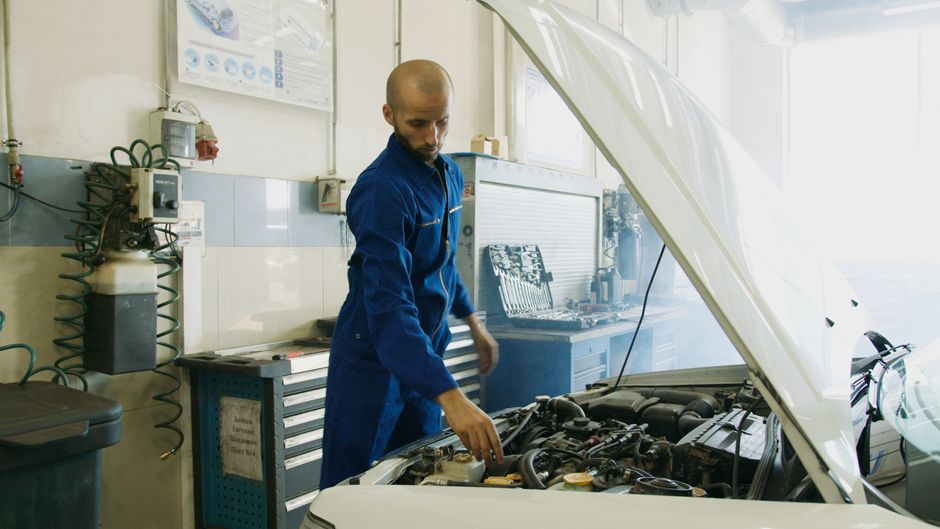 Mecânico examinando o motor de um carro no laboratório de manutenção automotiva.