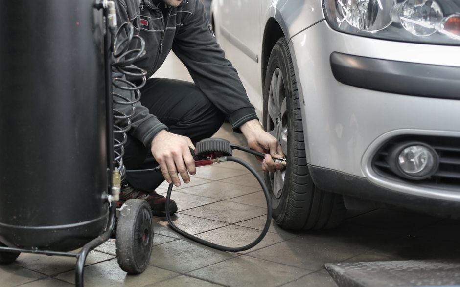 Imagem de um mecânico realizando manutenção em um carro, focando na troca ou inspeção dos pneus.