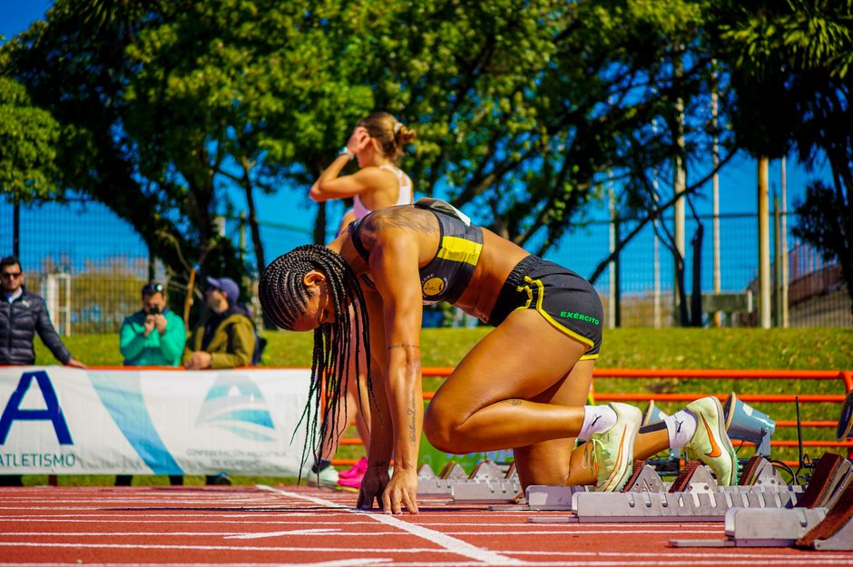 Atleta ocupada em posição de partida na pista de corrida em um evento ao ar livre, demonstrando preparação e foco na competição.