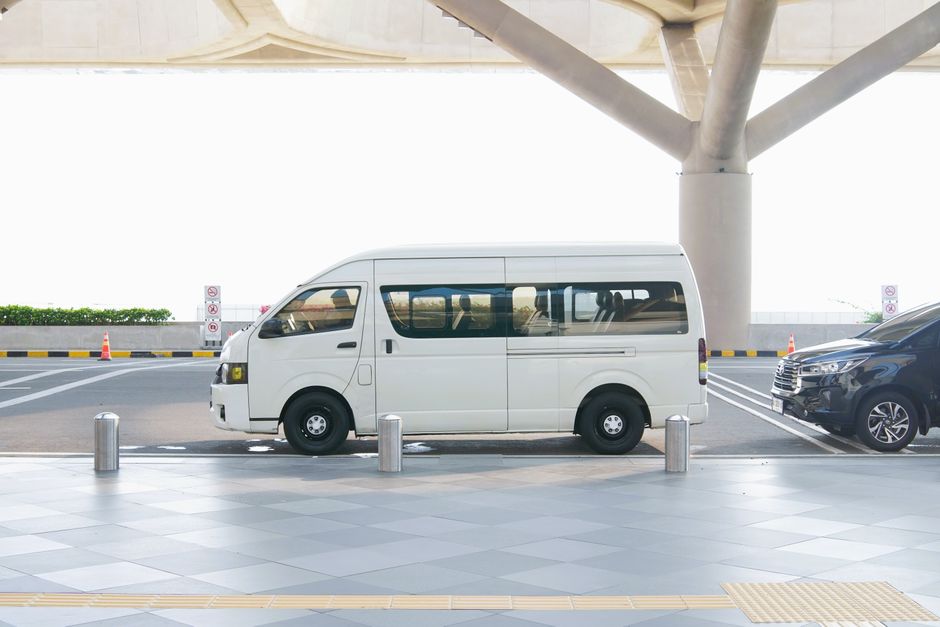 Imagem de um veículo de transporte, possivelmente de passageiros, estacionado em um local coberto, sob uma estrutura moderna, com sinalização de restrição ao lado.