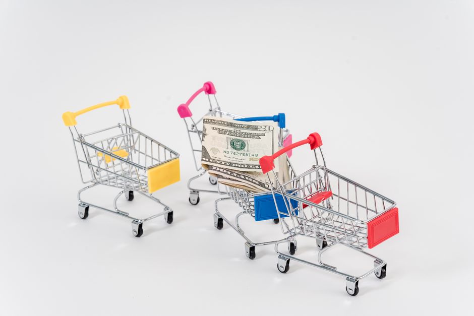 Imagem ilustrativa de compras com carrinhos de supermercado miniatura, representando consumo e mercado.