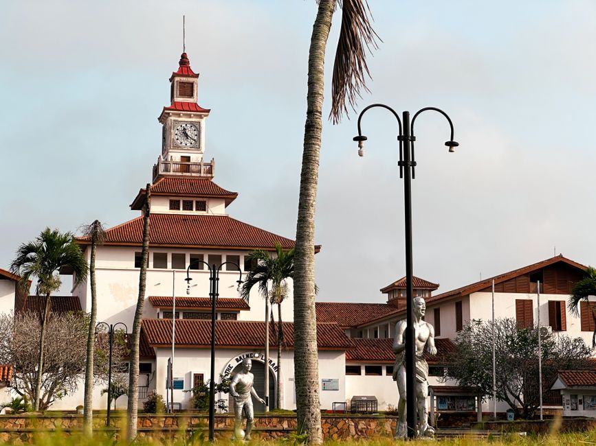 Imagem de um edifício histórico com torre, árvores e luminárias, evocando uma atmosfera de história e cultura urbana.