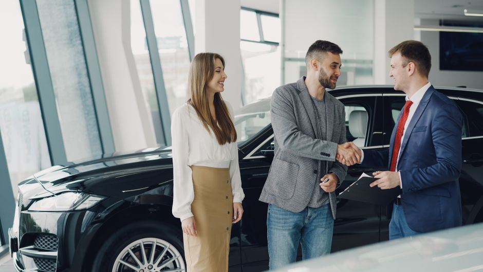 Homem e mulher fechando um negócio de compra de carro em uma concessionária moderna, com um funcionário apresentando o contrato.