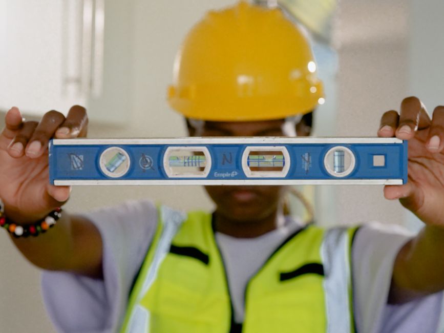 Profissional da construção civil utilizando nível para medir alinhamento em uma obra, simbolizando precisão e planejamento na construção