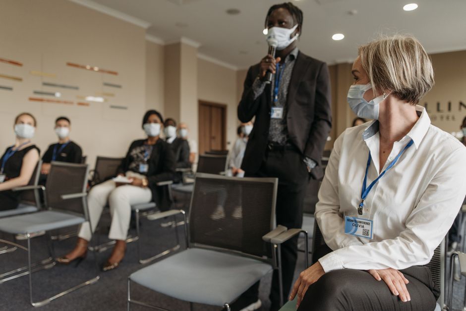 Profissionais participando de uma conferência ou seminário em um ambiente corporativo, com uso de máscara devido à pandemia.