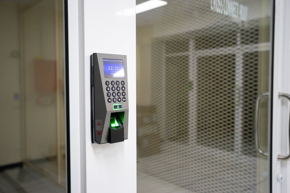 Sistema de controle de acesso com leitor de impressão digital instalado em uma porta de vidro, utilizado em ambientes corporativos ou de segurança.