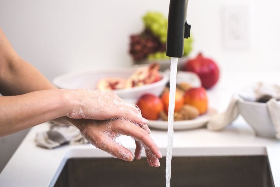 Pessoa lavando as mãos na cozinha, focando na higiene pessoal e limpeza no ambiente doméstico.