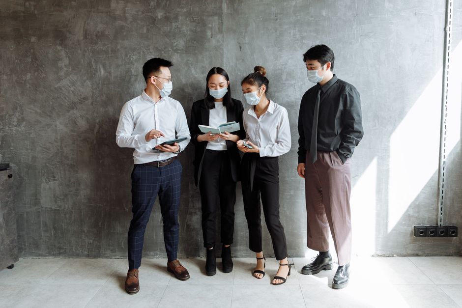 Grupo de pessoas usando máscaras faciais, envolvidos em uma discussão profissional, representando colaboração no ambiente de trabalho ou reunião empresarial.