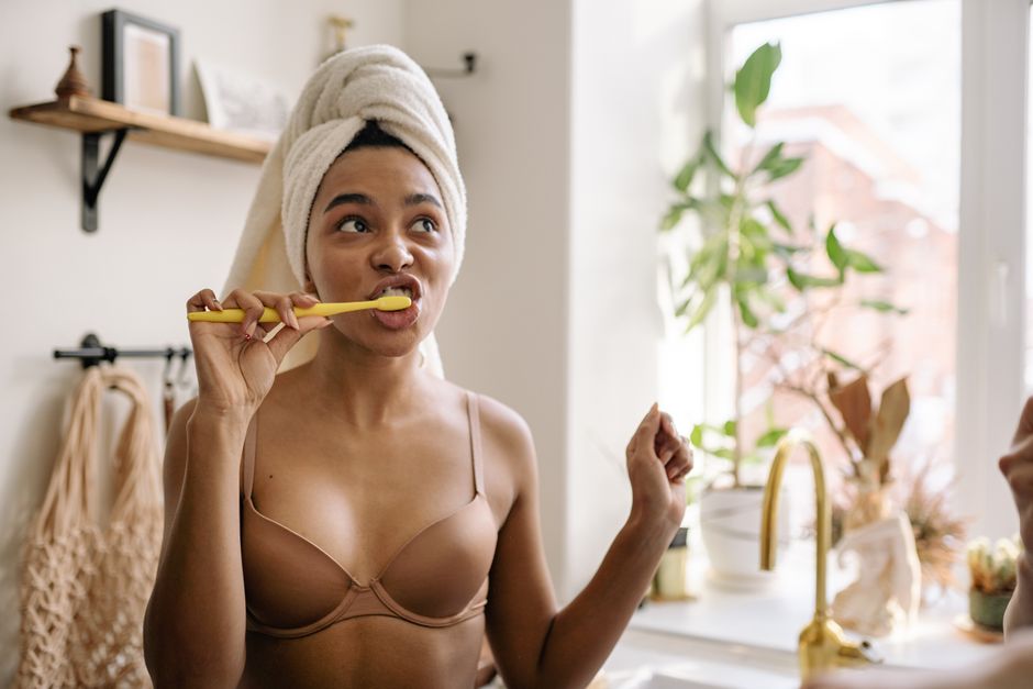 Mulher preparando-se para escovar os dentes em casa, com expressão de entusiasmo e rotina matinal.