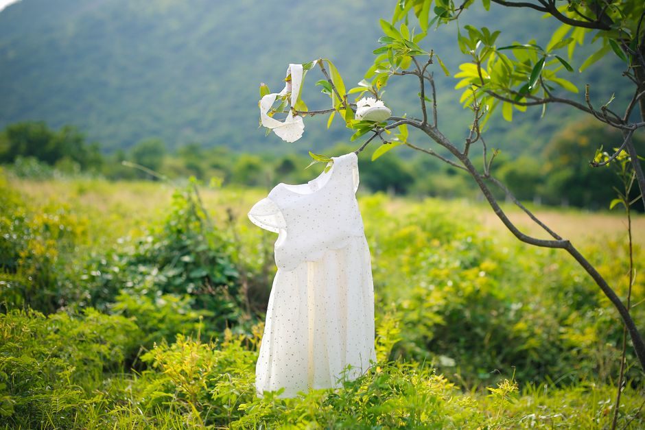 Vestuário infantil branco pendurado em um galho de árvore em um cenário natural, simbolizando a conexão entre crianças e o ambiente ao ar livre.