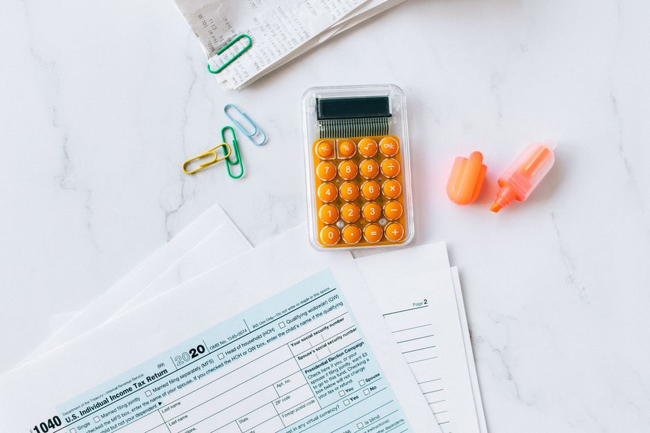 Imagem de materiais de escritório, incluindo uma calculadora, documentos de declaração de imposto e itens de papelaria, preparando-se para tarefas administrativas ou financeiras.